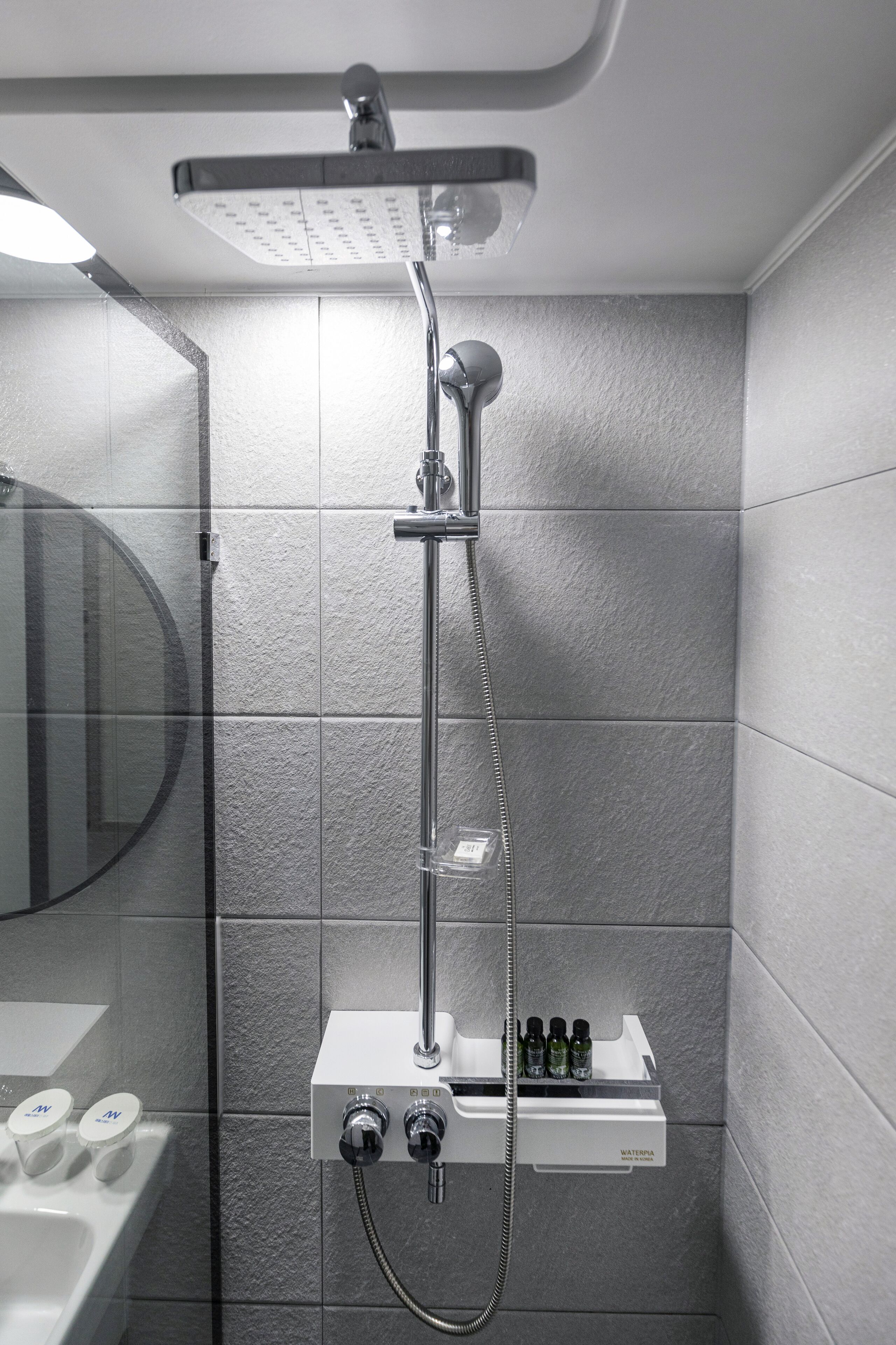 A modern bathroom with a shower, a mirror, and a soap dispenser.
