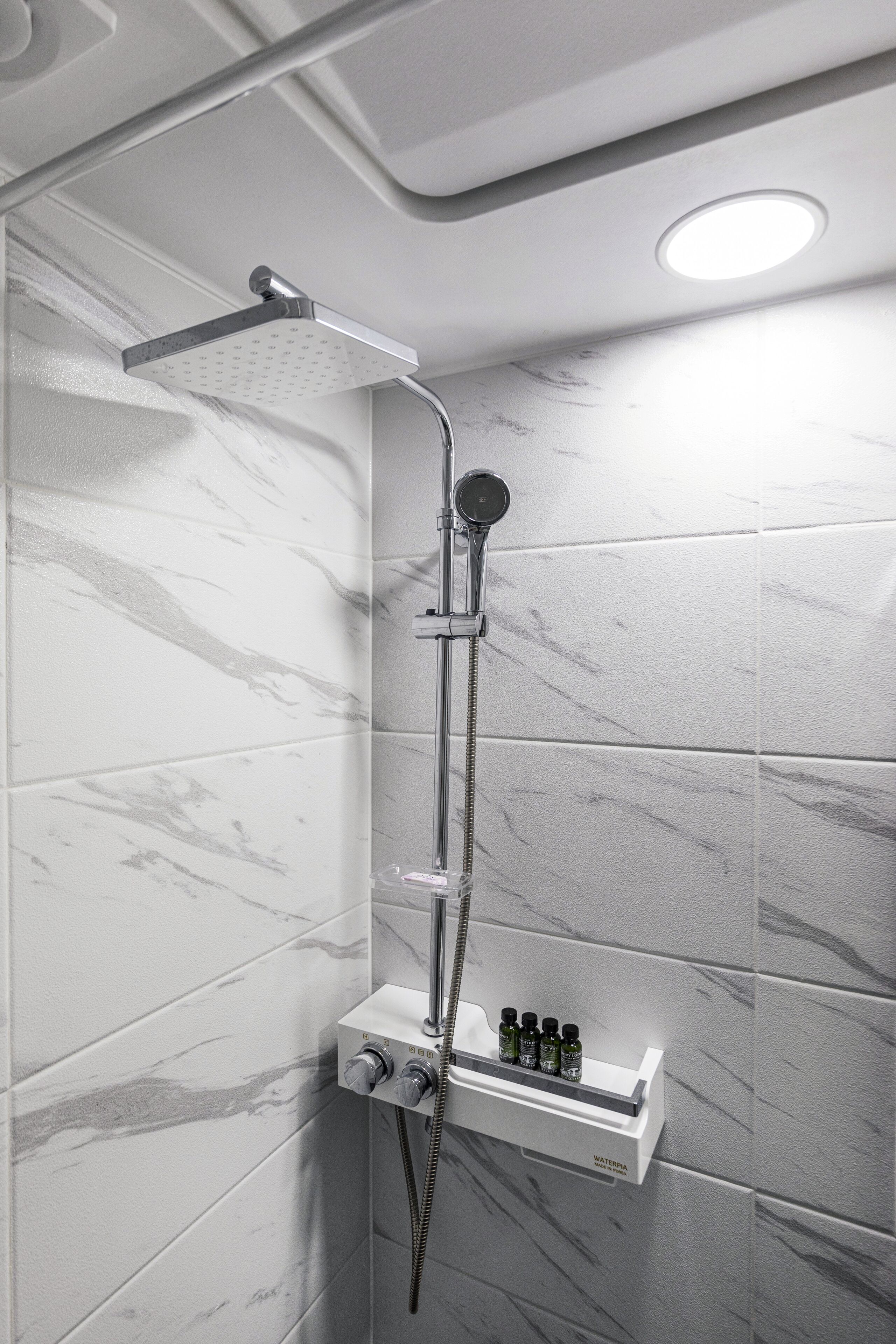 A modern shower with a handheld showerhead and a fixed overhead showerhead, mounted on a wall with a marble-like finish.