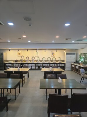 Un restaurante con varias mesas y sillas, una barra con una vitrina de platos, y una pared decorada con cuadros.