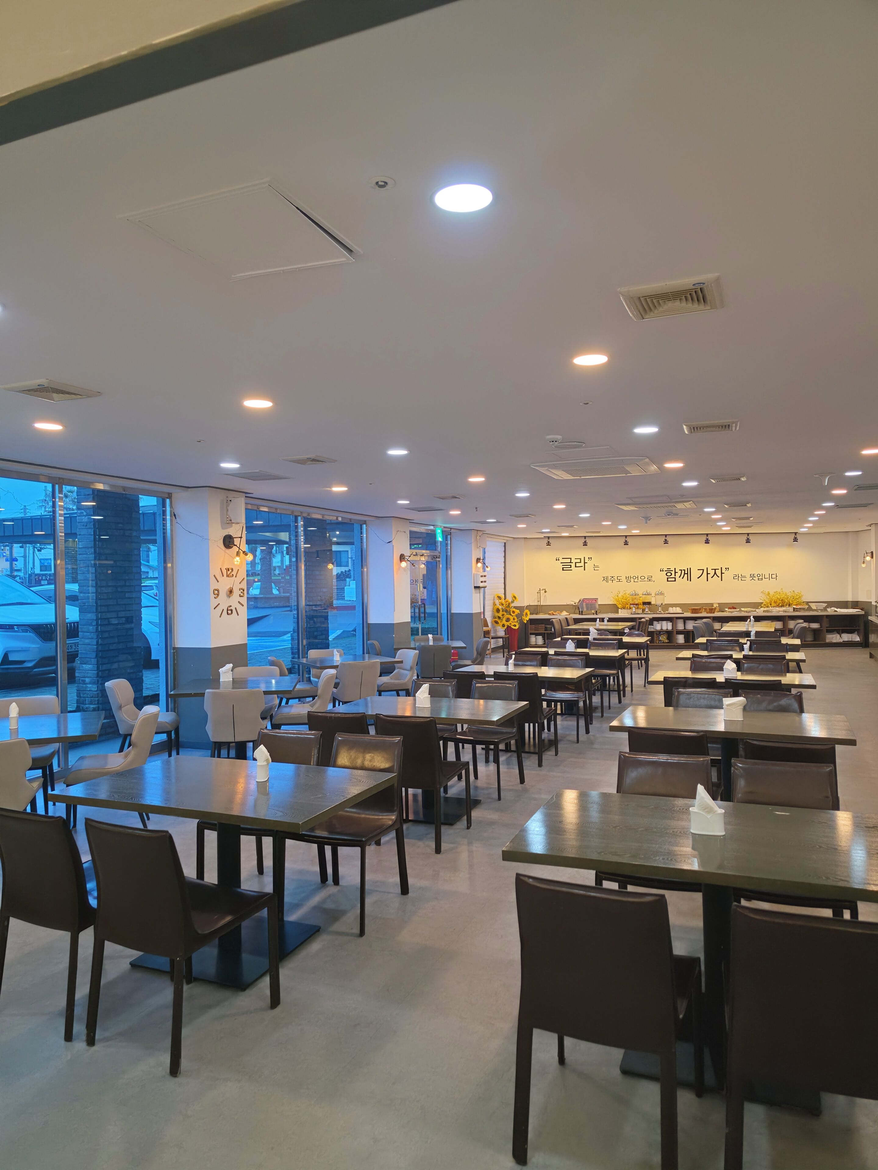 Un comedor amplio con varias mesas y sillas, ventanas grandes y un diseño moderno de techo.