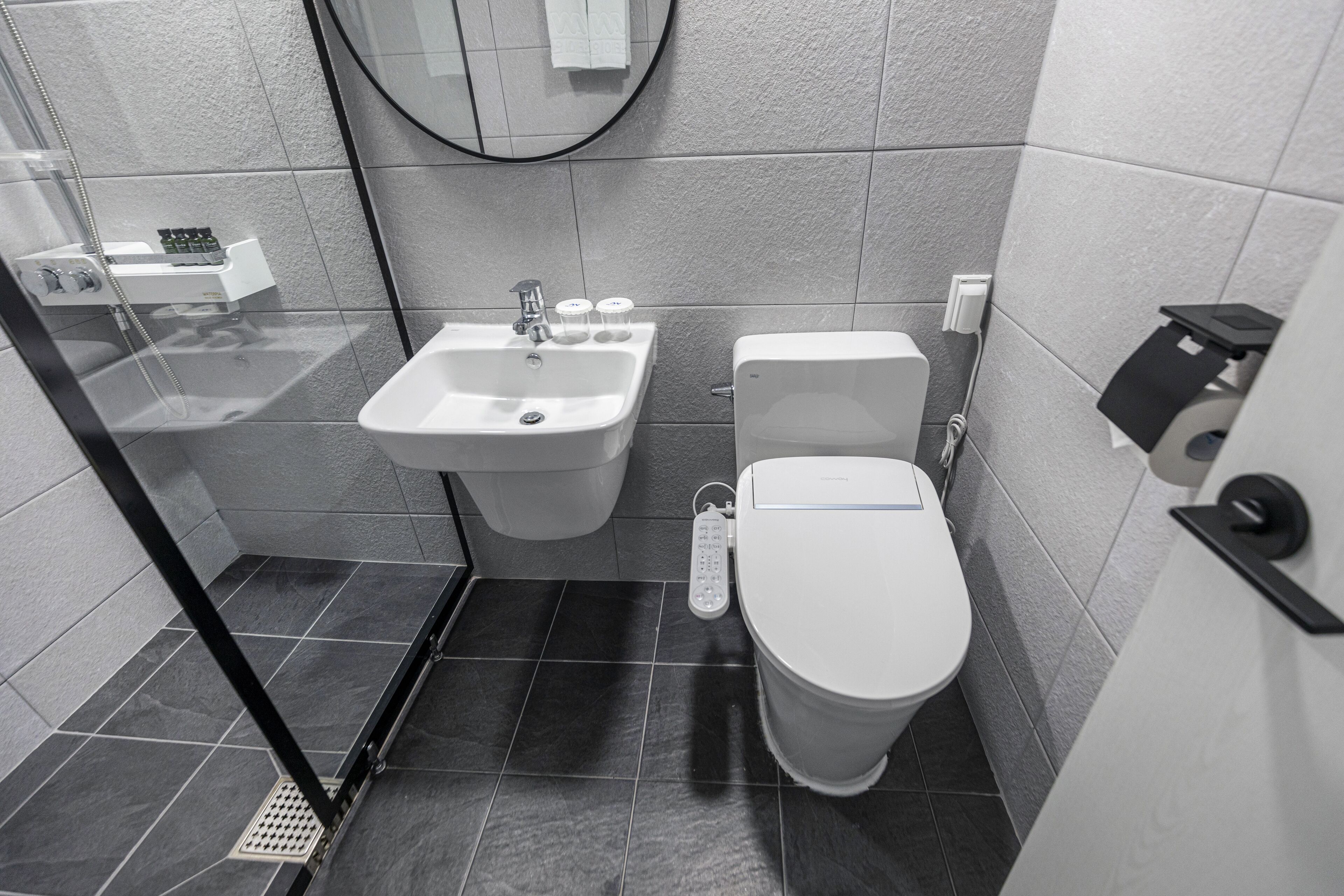 A modern bathroom with a glass-enclosed shower, a white sink with a soap dispenser, and a toilet.