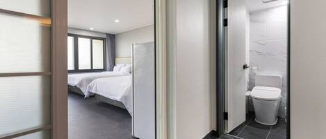 A hotel room with two beds, a bathroom with a toilet and sink, and a view of the outside through large windows.