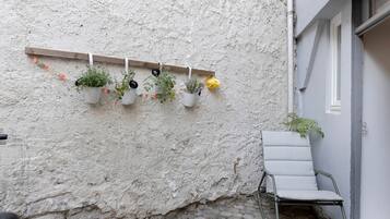 Un mur blanc à texture, agrémenté d’une étagère en bois où sont disposées des plantes en pot, et une chaise en métal.