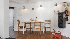 Un coin repas comprenant une table blanche, quatre chaises en bois, un fauteuil à bascule rouge et une étagère murale où sont disposés divers objets.