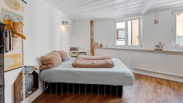 Une chambre à coucher avec un lit, un radiateur, une fenêtre et un mur sur lequel est accroché un calendrier.