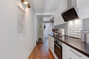 Eine Küche mit Herd, Backofen und Mikrowelle. Der Boden ist aus Holz und die Rückwand ist mit weißen Fliesen versehen.
