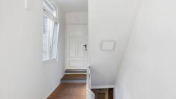 Un couloir étroit avec un plancher en bois, des murs blancs et une porte blanche au fond.