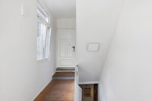 Een smalle gang met houten vloer, witte muren en een witte deur aan het einde.