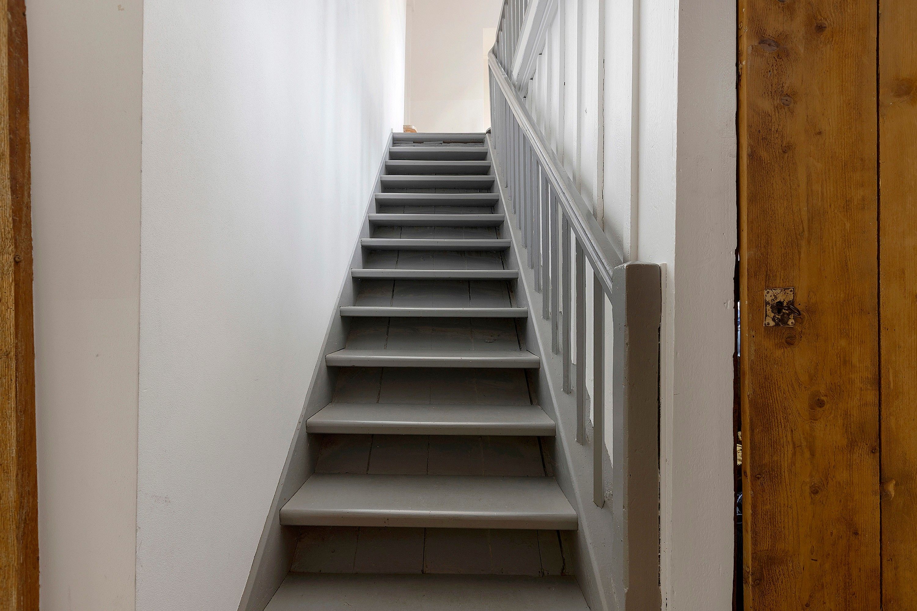 Una escalera estrecha con baranda de madera y paredes blancas.