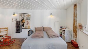 Une chambre à coucher comprenant un lit, une chaise, une étagère avec des livres et un mur décoré d’œuvres d’art.