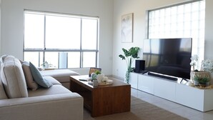 Un salon moderne avec un canapé, une table basse, un téléviseur et de grandes fenêtres.