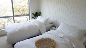 Une chambre avec deux lits, du linge de lit blanc, une tête de lit en osier et une vue sur la verdure.