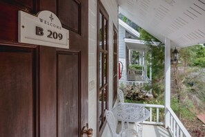 A wooden door with a 'Welcome B209' sign, a white porch with a table and chairs, and a view of a white house with a balcony. - Sakarin Valley Resort & Restaurant (Kanchanaburi)