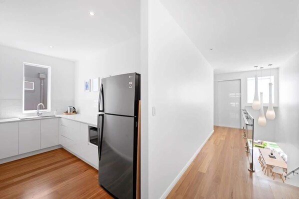 A modern kitchen with white cabinetry, a black refrigerator, and a wooden floor.