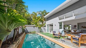 Ein modernes Haus mit Swimmingpool, Sitzgelegenheit im Freien und tropischen Pflanzen.
