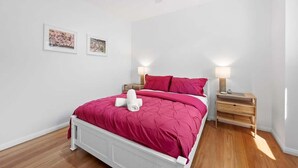 Ein Schlafzimmer mit einem weißen Bett, rosa Bettwäsche, zwei Nachttischlampen und einem Deckenventilator.