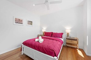 A bedroom with a white bed, pink bedding, two bedside lamps, and a ceiling fan.