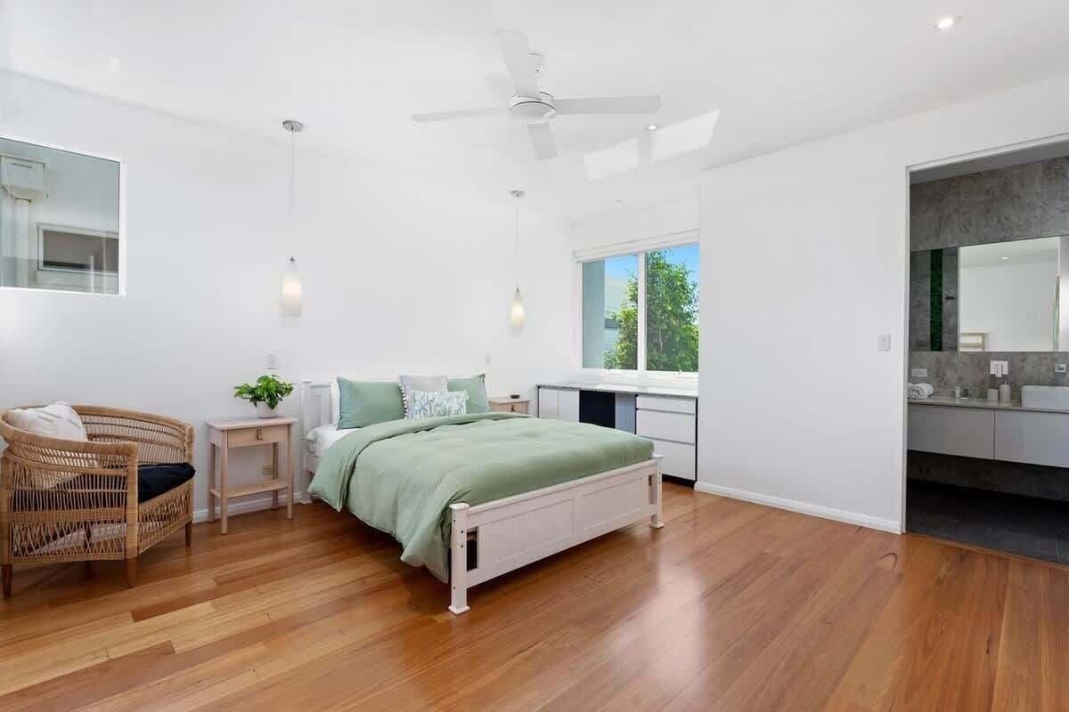 A modern bedroom with a bed, bedside tables, a chair, and a large window.