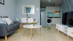 A modern living room with a grey sofa, a round coffee table, and a TV on a white cabinet. - Classy 2BR Apartment at Menteng Park with City View (Jakarta)