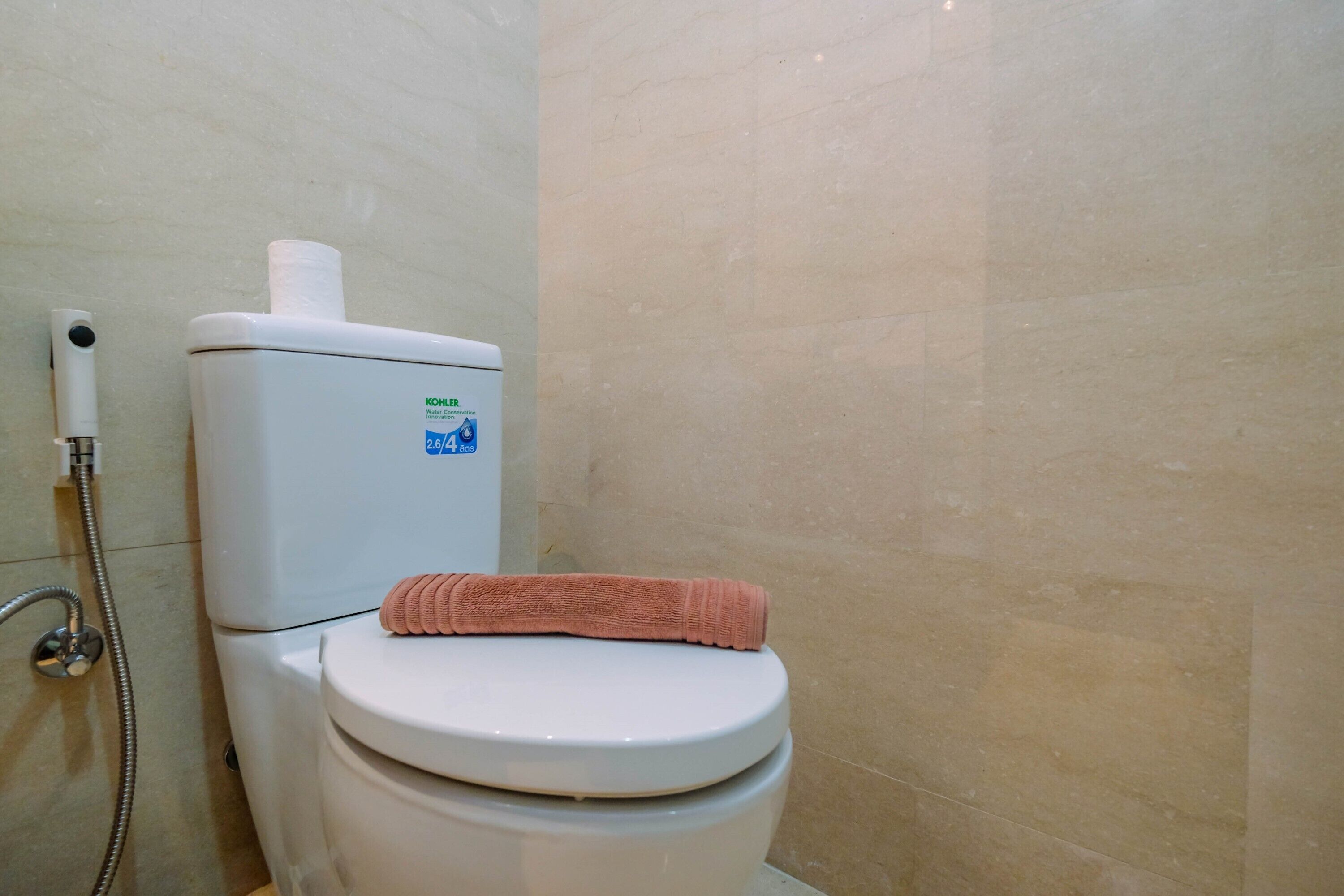 A white toilet with a towel on top, a water heater, and a shower hose.