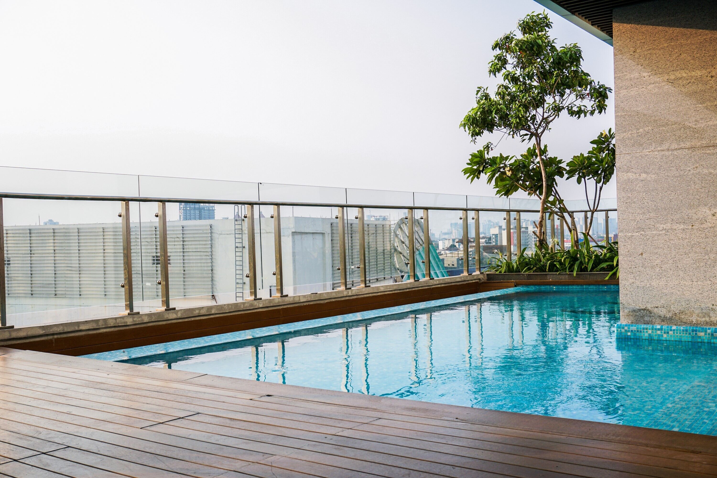 Una piscina en la azotea con terraza de madera y barandilla de cristal.