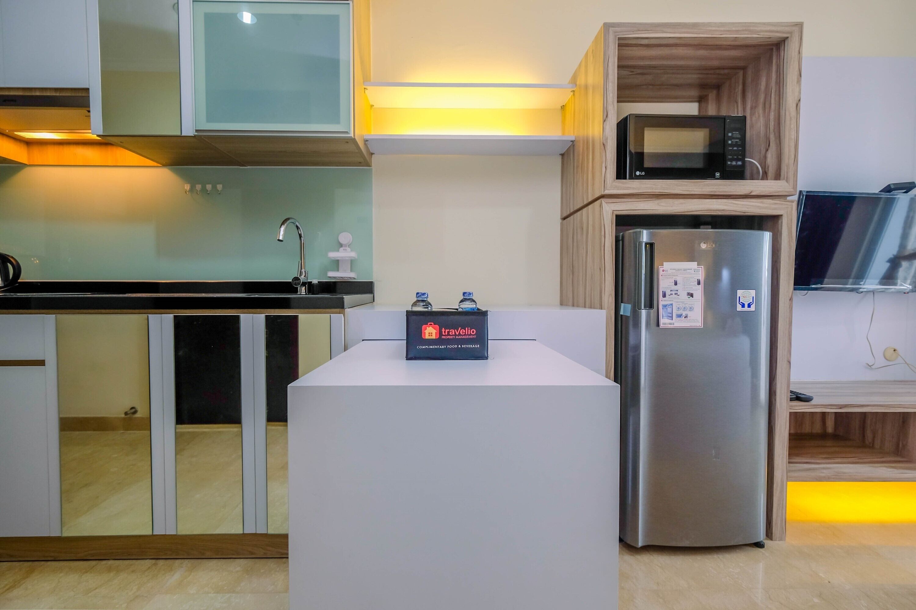 Una cocina moderna con un refrigerador de acero inoxidable, un microondas sobre una repisa de madera y un espacio para alimentos y bebidas de un viajero.