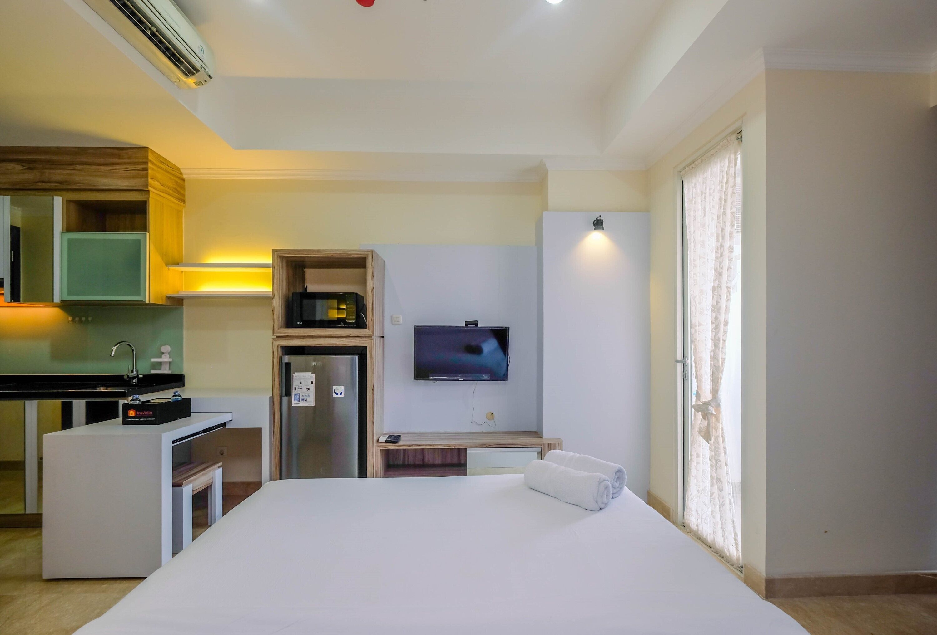 A hotel room with a bed, a TV, a small kitchenette, and a bathroom.