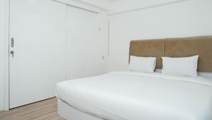 Un dormitorio con cama, piso de madera, puerta blanca y cabecera marrón.