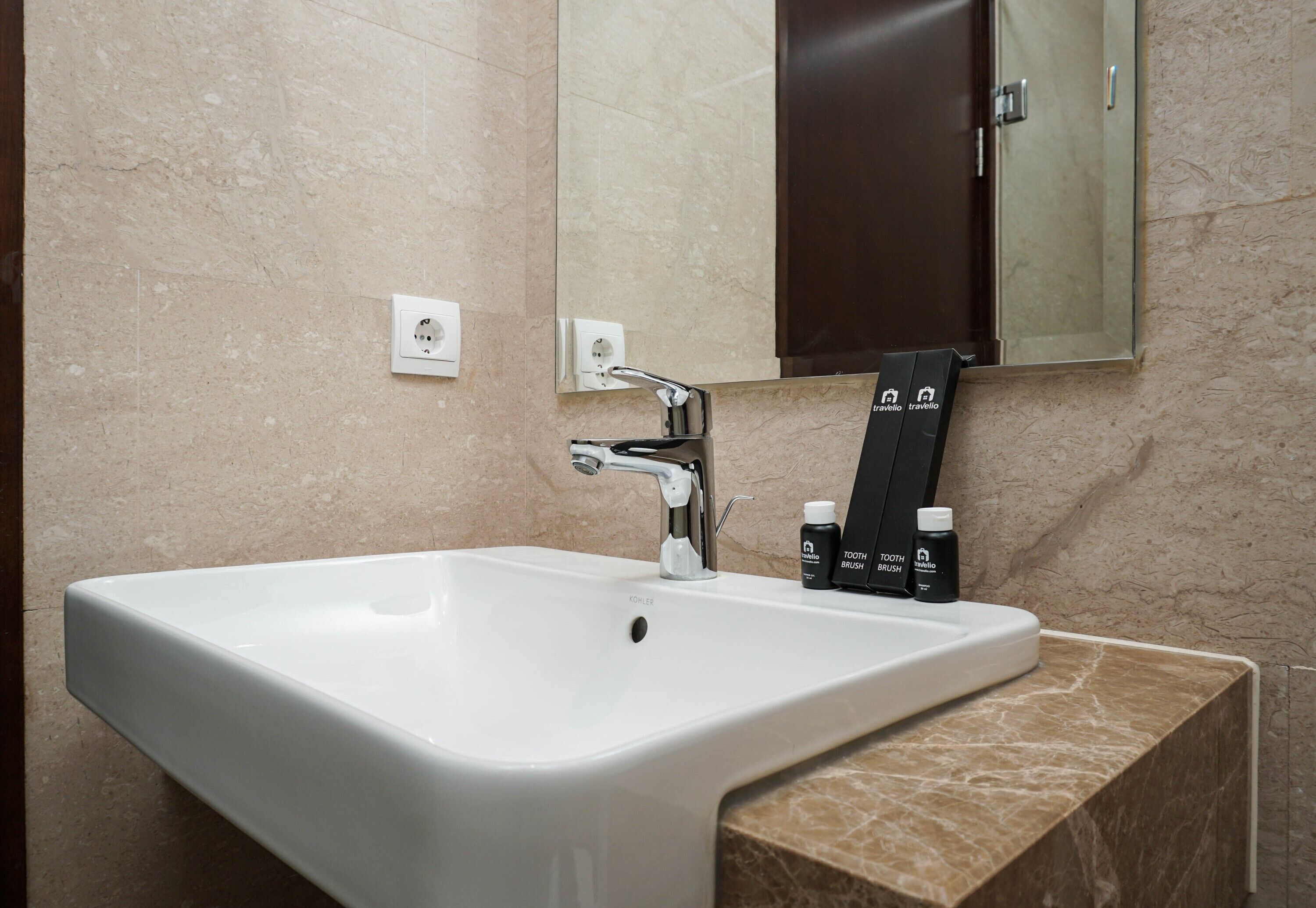 Une salle de bain moderne avec un lavabo blanc, un robinet chromé et un plan de toilette en marbre. On y trouve deux brosses à dents et un tube de dentifrice posés sur le plan de toilette.