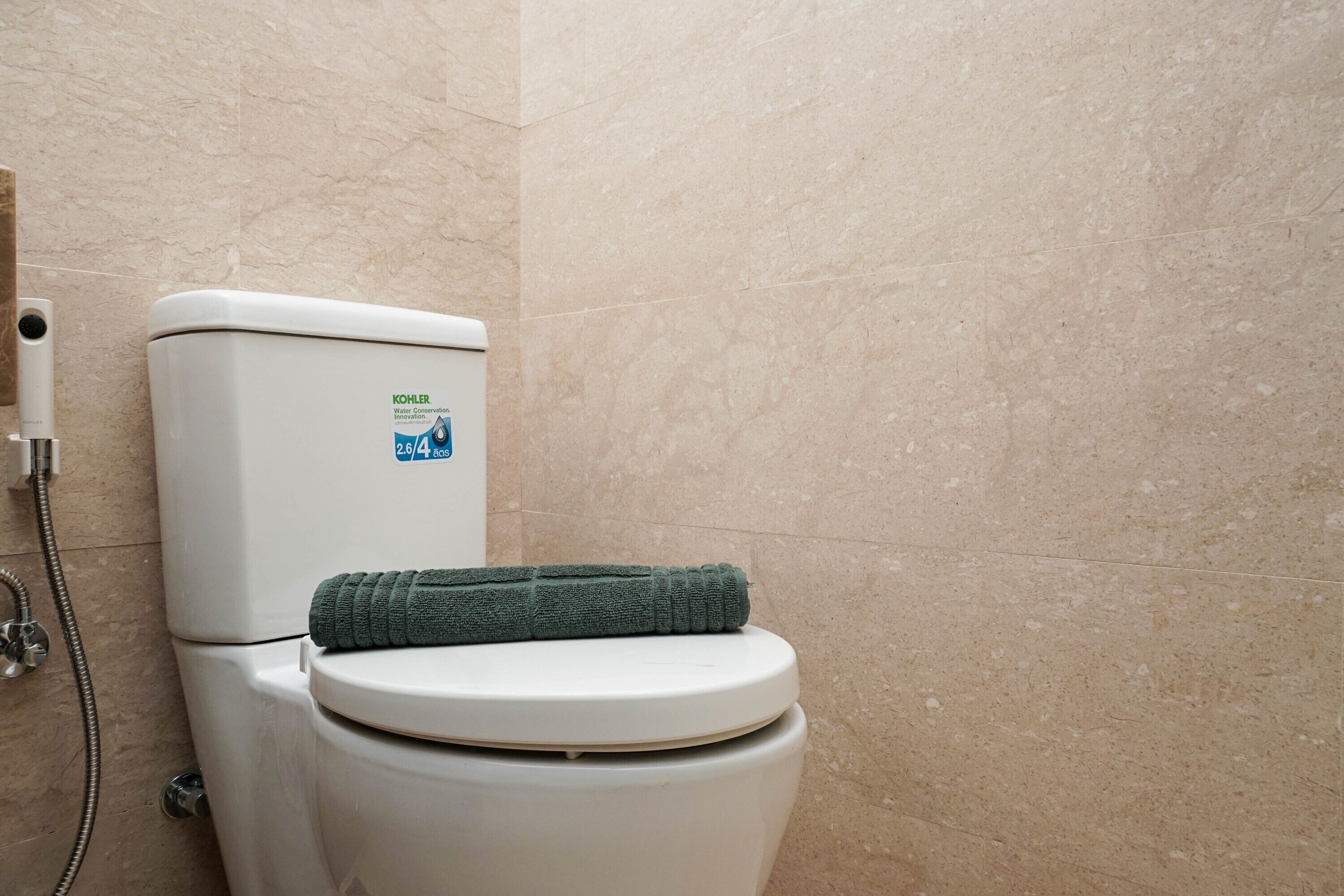 Des toilettes portant le label de Kohler en matière d’économie d’eau, et une serviette verte posée sur le couvercle.