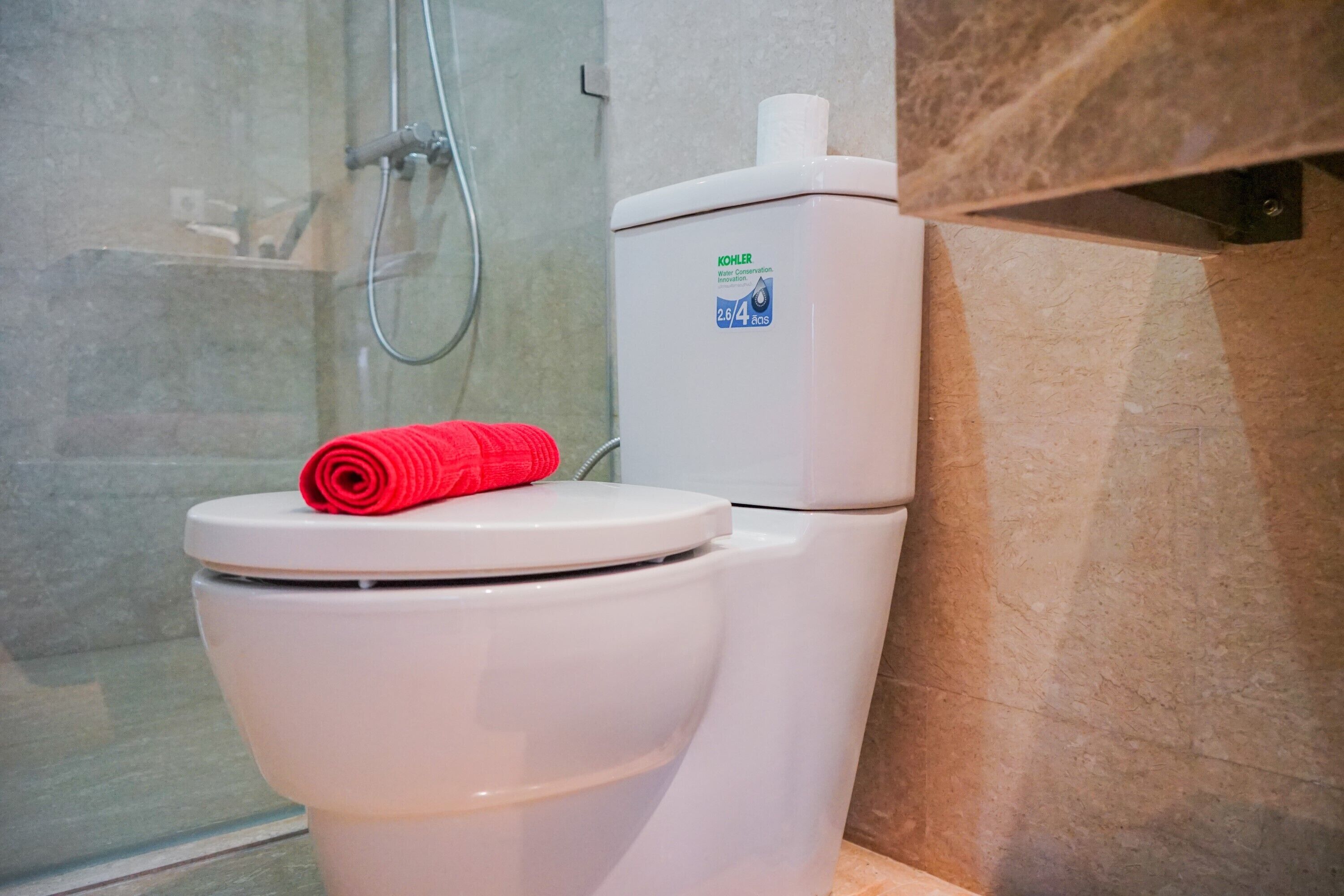 A white toilet with a red towel on the lid, a water conservation sticker, and a shower area with a glass door.