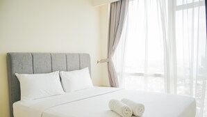 A neatly made bed with white linens and two rolled towels, a grey upholstered headboard, and a view through sheer curtains. - Chic and Cozy 2BR Apartment at Menteng Park (Jakarta)