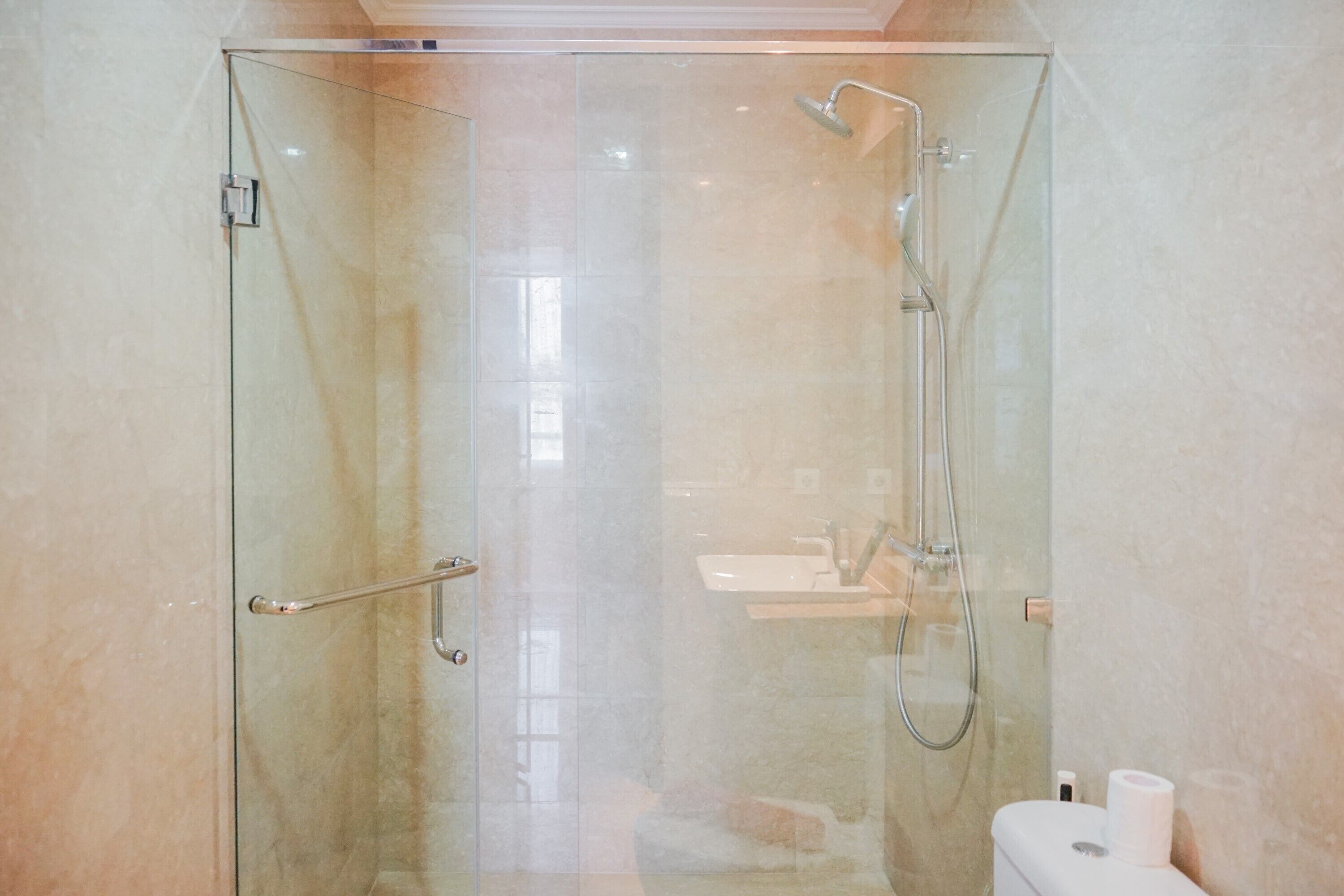 Une douche fermée par des parois en verre, dotée d’un pommeau de douche à main et d’un robinet à main.