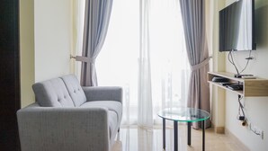 A modern living room with a grey sofa, a glass coffee table, a flat-screen TV mounted on the wall, and a large window with sheer curtains. - Chic and Cozy 2BR Apartment at Menteng Park (Jakarta)