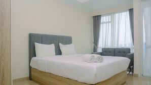 A modern hotel room with a wooden bed frame, white bedding, and a grey upholstered chair. - Elegant and Stylish Studio Menteng Park Apartment (Jakarta)