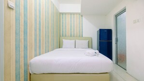 A neatly made bed with white linens and pillows, a blue refrigerator, and striped wallpaper on the walls.