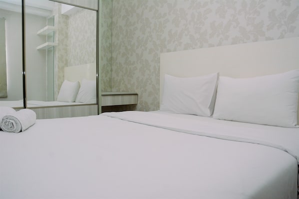 A hotel room with a neatly made bed, a large mirror, and a patterned wallpaper.