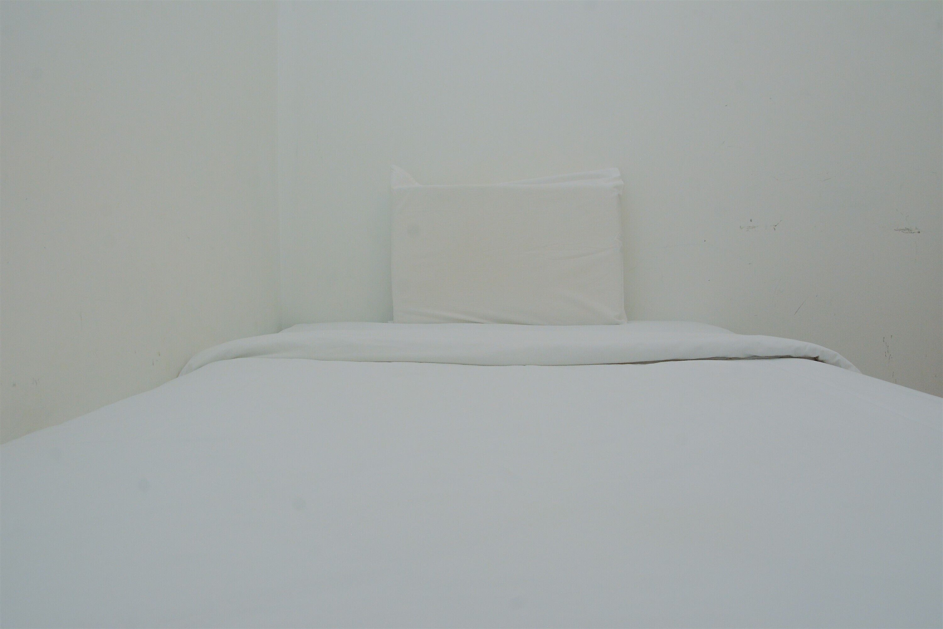 A small, plain room with a single bed and a pillow.