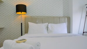 A neatly made bed with white linens, a remote control, and rolled towels on a hotel room.