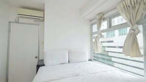 A hotel room with a bed, a door, and a window with curtains.