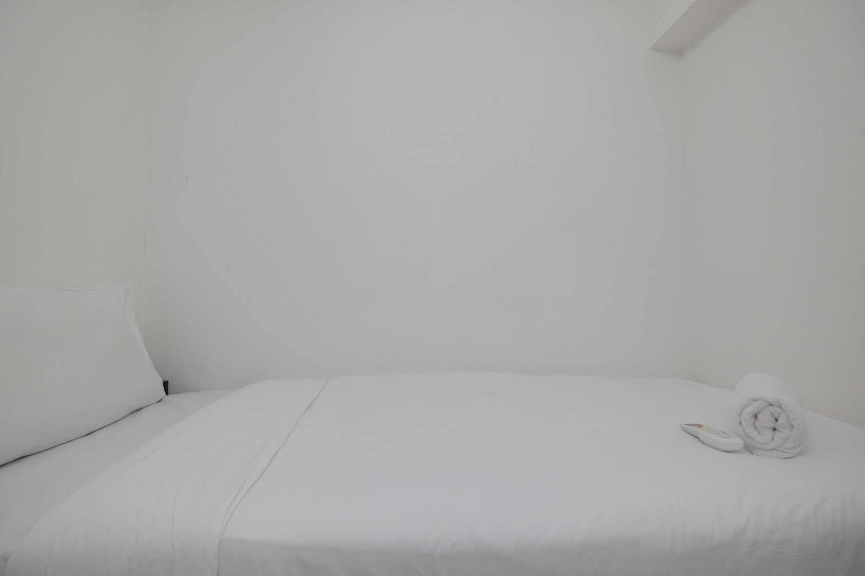 Habitación blanca con cama, almohada y una toalla enrollada.