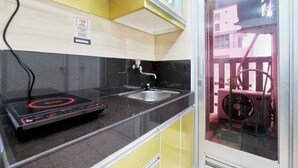 A compact kitchen with a black induction cooktop, a stainless steel sink, and a yellow cabinet.