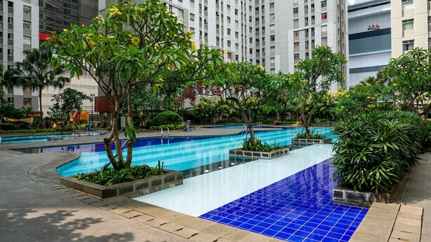 A modern residential building with a swimming pool area, surrounded by greenery and palm trees.