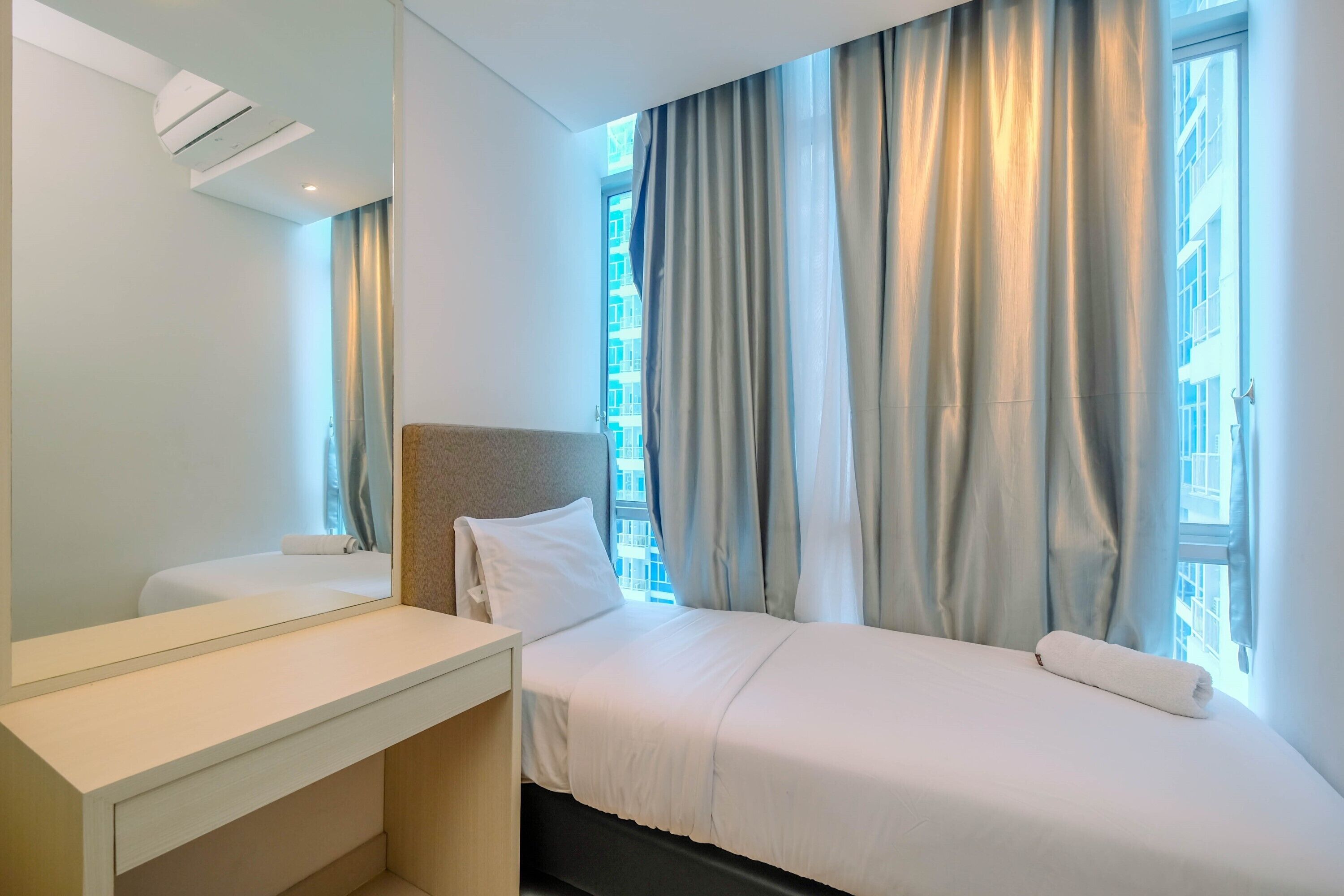 A hotel room with a bed, a bedside table, a mirror, and a window with curtains.