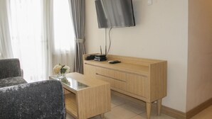 Hotellihuone, jossa on seinälle asennettu taulutelevisio, puinen työpöytä, tuoli ja pieni pöytä, jonka päällä on maljakko täynnä kukkia.