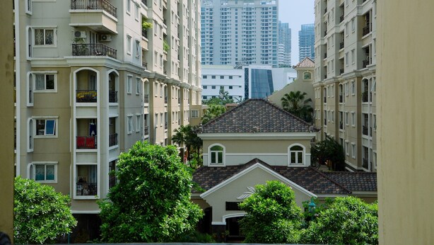 Un immeuble résidentiel à plusieurs étages, doté de balcons et d’une cour intérieure, avec un gratte-ciel moderne en arrière-plan.