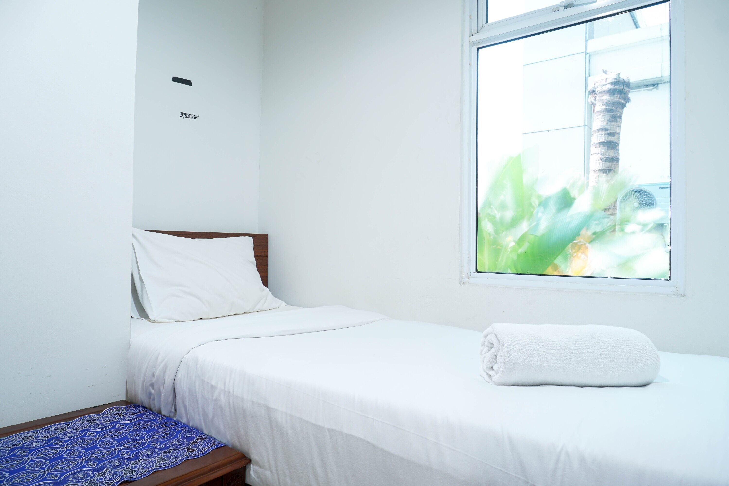 A single bed with white bedding, a blue patterned throw, and a white towel on the side.