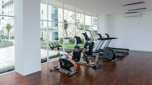 Ein Fitnessstudio mit Trainingsgeräten, großen Fenstern und Blick auf Gebäude sowie Grünflächen.