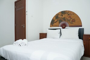 A neatly made bed with white linens, a wooden headboard, and a decorative fan. - Luxurious and Elegant 3BR Vittoria Apartment (Jakarta)
