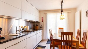 A modern kitchen with a dining area, including a table and chairs, and a window with curtains. - Hauswurz by Interhome (Gwatt (Thun))